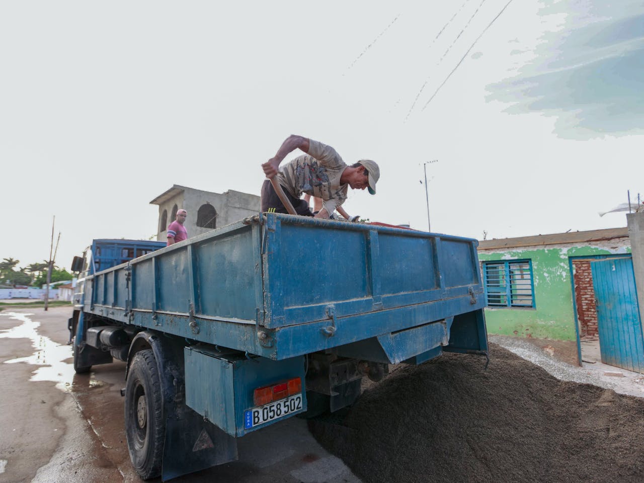 A construction worker unloads sand from a blue truck at an outdoor site, showcasing manual labor.
