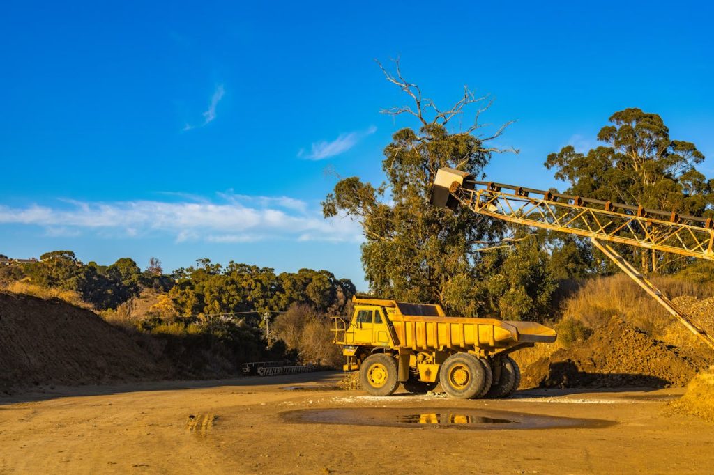 A large dump truck and conveyor in a quarry under a bright blue sky.