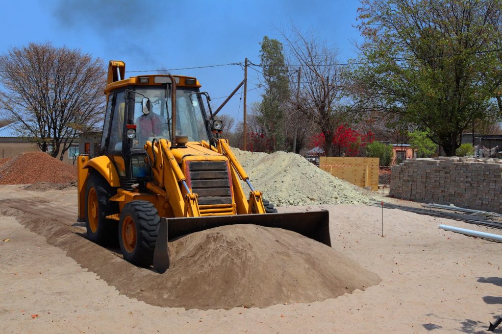 A yellow backhoe loader at a construction site moving sand on a clear day.